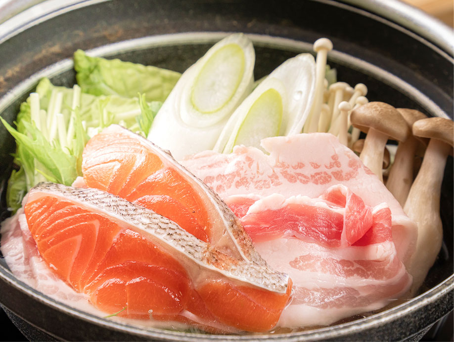 鮭や豚肉、野菜が並ぶ鍋料理の具材の盛り付け