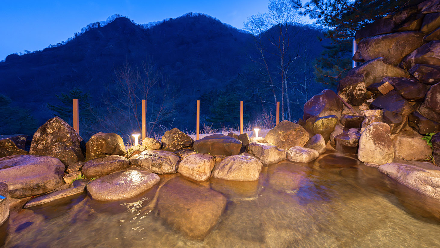 夜ライトアップされた自然の岩風呂と山の風景